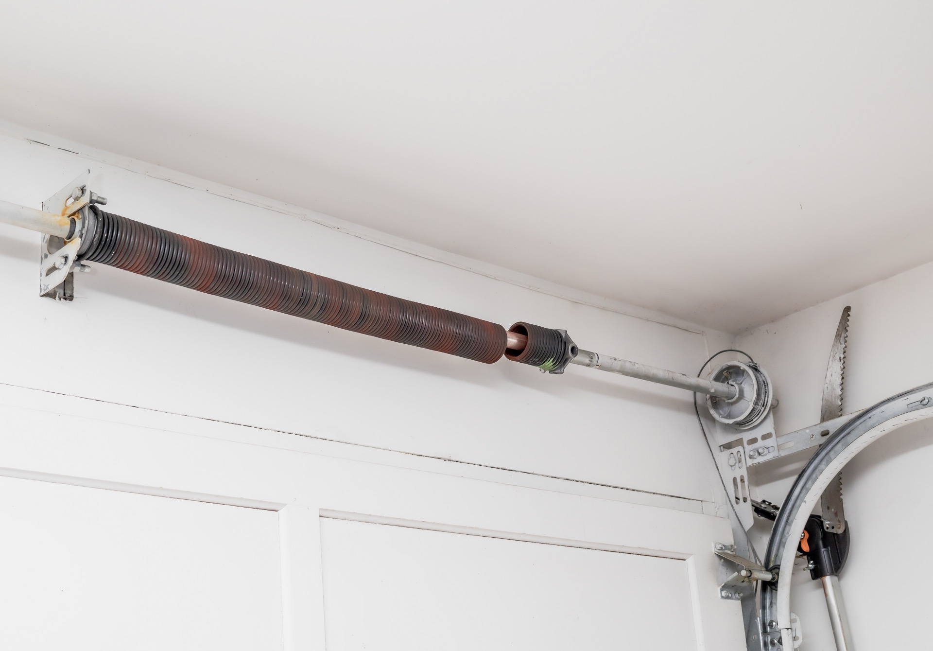 Broken garage door spring or torsion spring from overhead sectional door inside white garage.